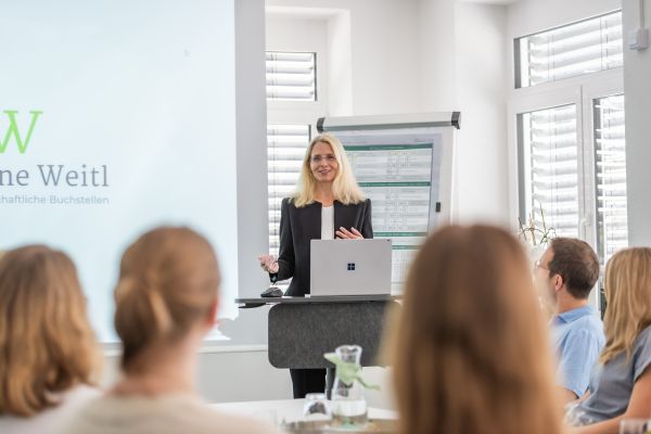 Frau Dr. Weitl in einer Teambesprechung vor einem Flipchart und einer Beamerwand zum Thema Unternehmensberatung