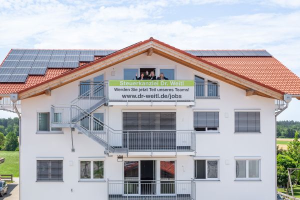 Außenansicht des Firmensitzes. Frau Dr. Weitl winkt mit Angestellten vom Balkon